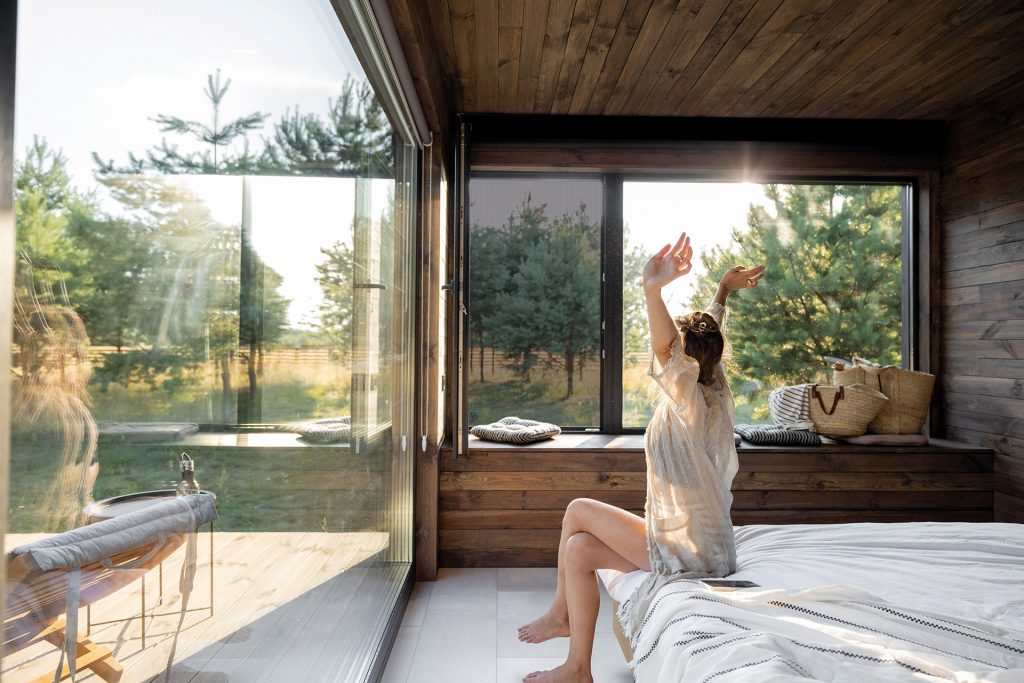 Femme se réveillant dans une chambre avec de grandes baies vitrées